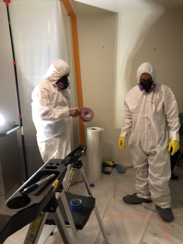 a couple of people wearing white hazmat suits and masks doing mold remediation services in orange county